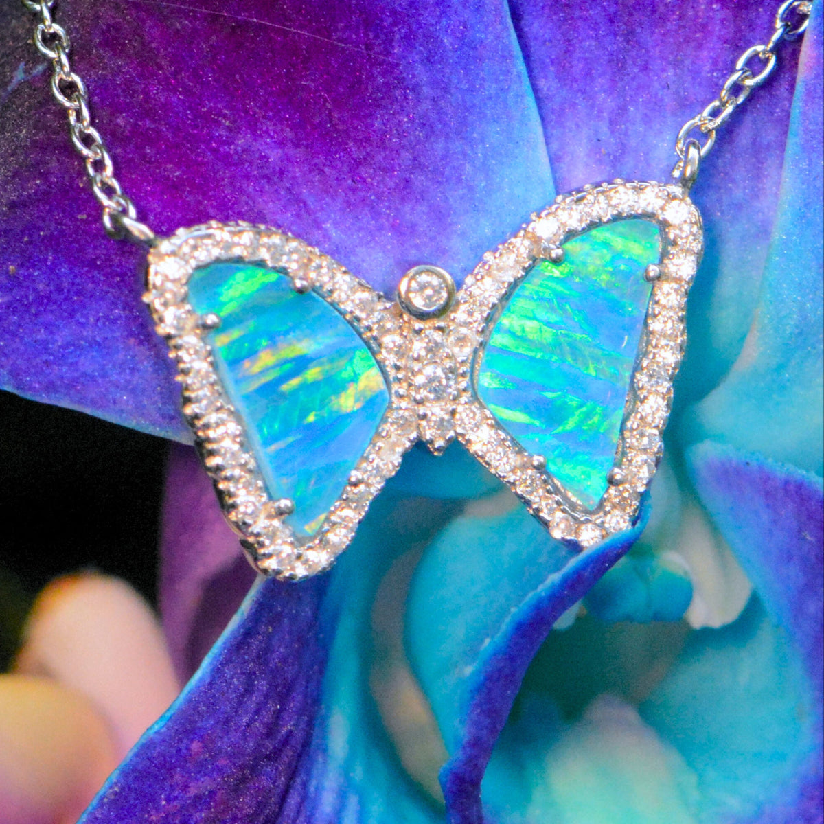 Butterfly-shaped necklace with blue and green opal stones on a purple flower background