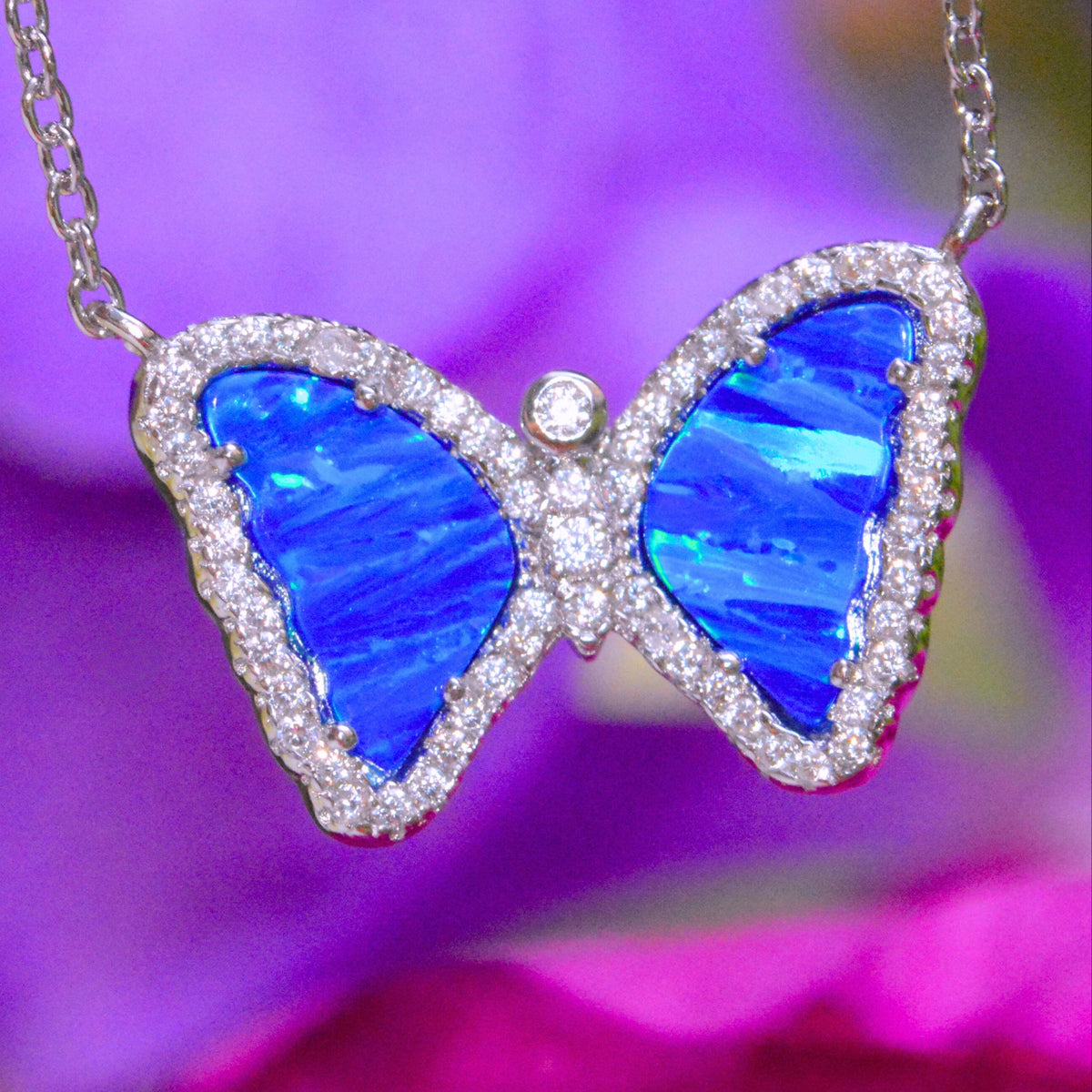 Butterfly-shaped necklace with blue opal wings and diamond accents against a blurred purple background