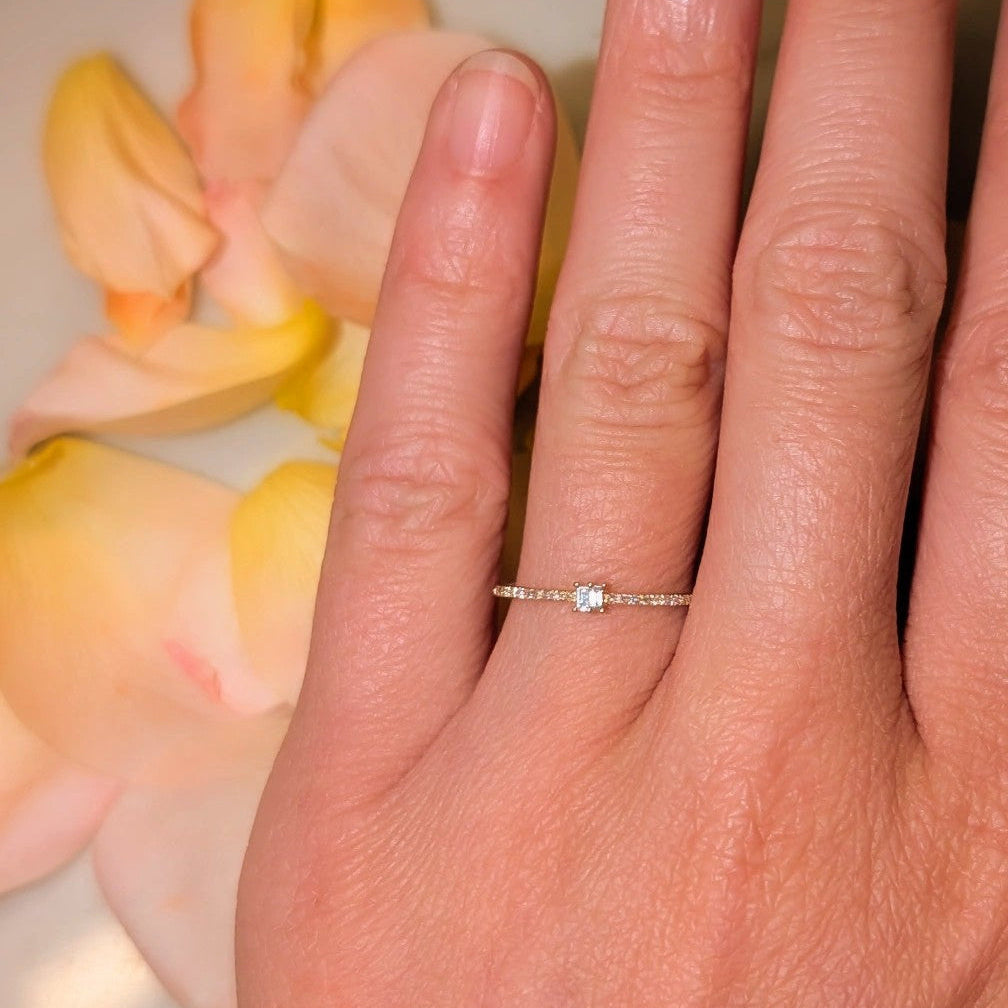 Hand wearing a ring with a small blue gemstone against a soft focus background