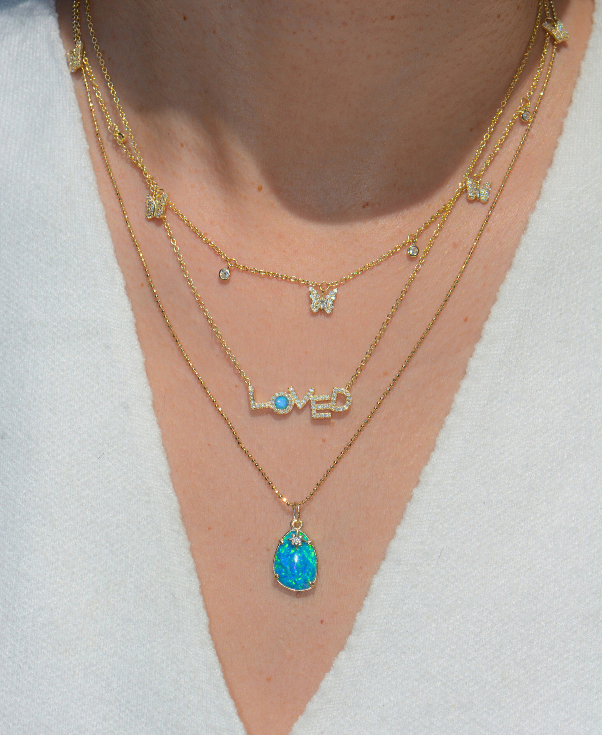 Close-up of a person wearing multiple gold necklaces with various pendants on a white background