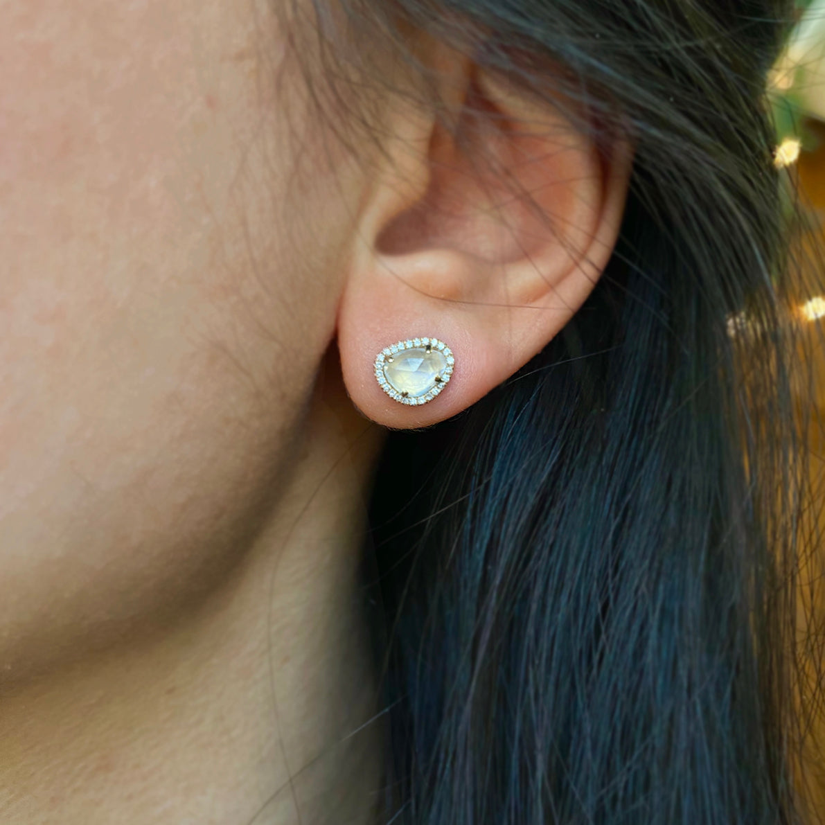A pair of pebble-shaped moonstone earrings with halo settings of smaller diamonds around them, in a gold mounting.